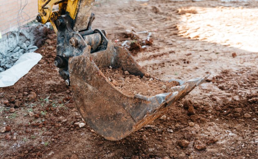 Shovel machine on construction site with worker working with pneumatic hammer on background